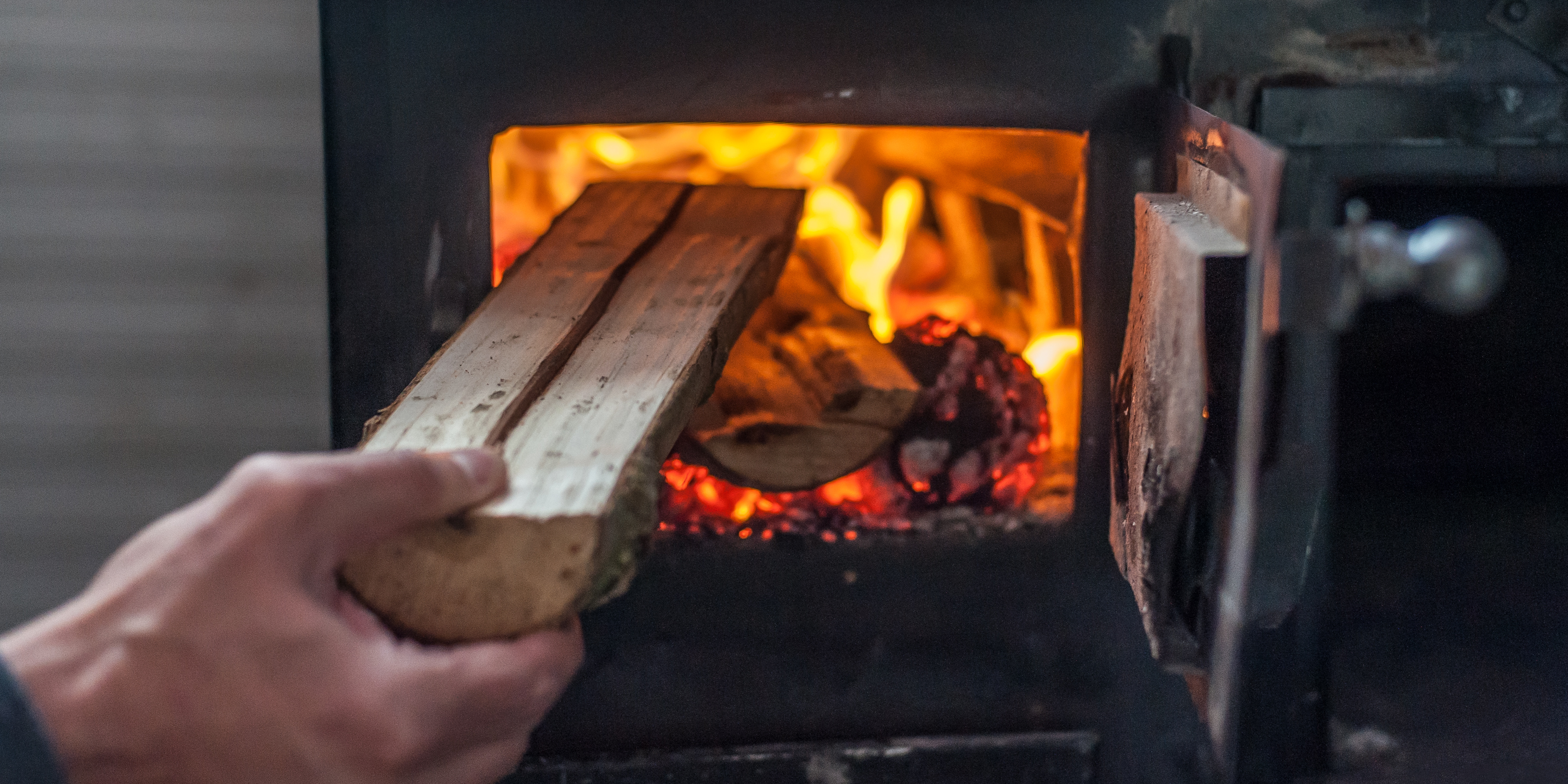 Den optimalen Zeitpunkt zum Nachlegen im Kamin erkennen Hand legt ein Stück Holz in den brennenden Ofen
